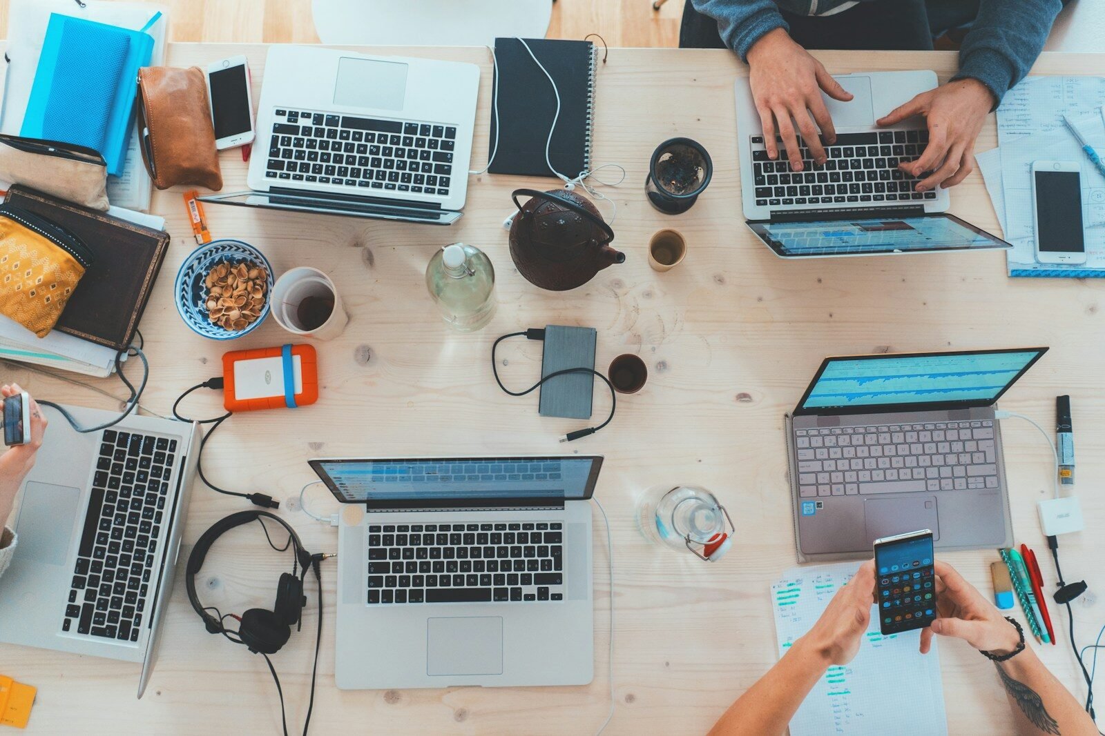 people sitting down near table with assorted laptop computers and other tech